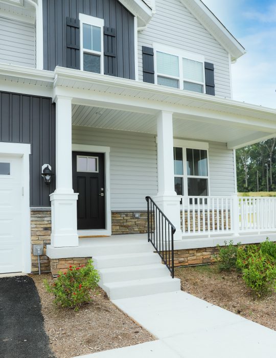 close up of home with grey board and batten siding and vertical siding with wrap around white porch